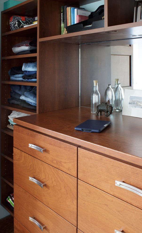 Photo of a mid-sized contemporary gender-neutral built-in wardrobe in New York with flat-panel cabinets, medium wood cabinets and light hardwood floors.