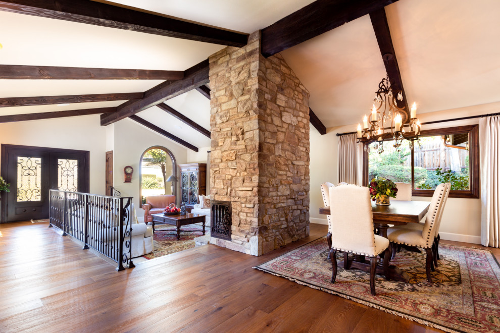 Photo of a mid-sized mediterranean open plan dining in Los Angeles with beige walls, medium hardwood floors, a corner fireplace, a stone fireplace surround, brown floor and exposed beam.