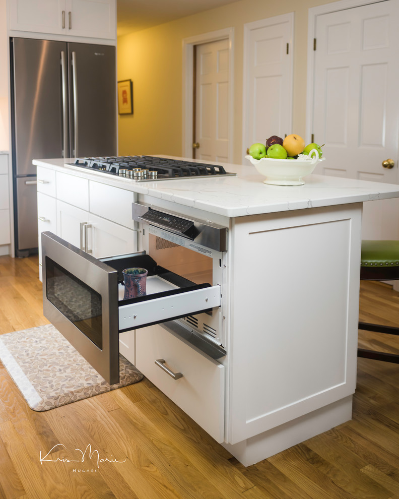 Inspiration for a mid-sized timeless medium tone wood floor kitchen remodel in Boston with an undermount sink, recessed-panel cabinets, white cabinets, granite countertops, white backsplash, mosaic tile backsplash, stainless steel appliances, an island and white countertops