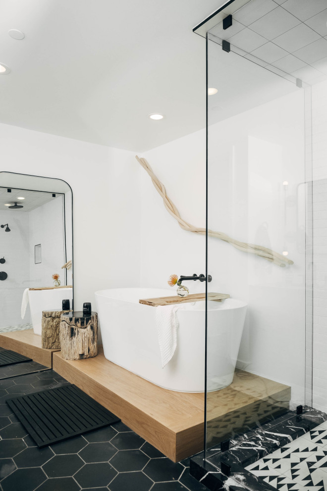 Photo of a large contemporary master bathroom in Other with a freestanding tub, a corner shower, white tile, white walls, cement tiles, black floor and a hinged shower door.
