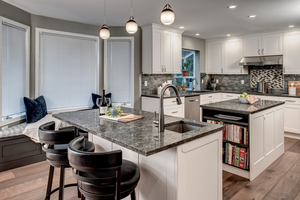 Photo of a medium sized traditional l-shaped kitchen/diner in Seattle with a double-bowl sink, shaker cabinets, white cabinets, engineered stone countertops, grey splashback, ceramic splashback, stainless steel appliances, medium hardwood flooring, multiple islands, brown floors and grey worktops.