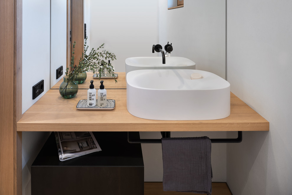 Inspiration for an expansive scandinavian powder room in Munich with mirror tile, white walls, light hardwood floors, a vessel sink, wood benchtops, brown floor and beige benchtops.