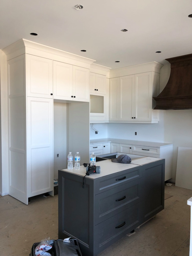 Design ideas for a mid-sized country u-shaped eat-in kitchen in Toronto with a farmhouse sink, shaker cabinets, white cabinets, quartzite benchtops, white splashback, ceramic splashback, stainless steel appliances, light hardwood floors, with island, beige floor and white benchtop.