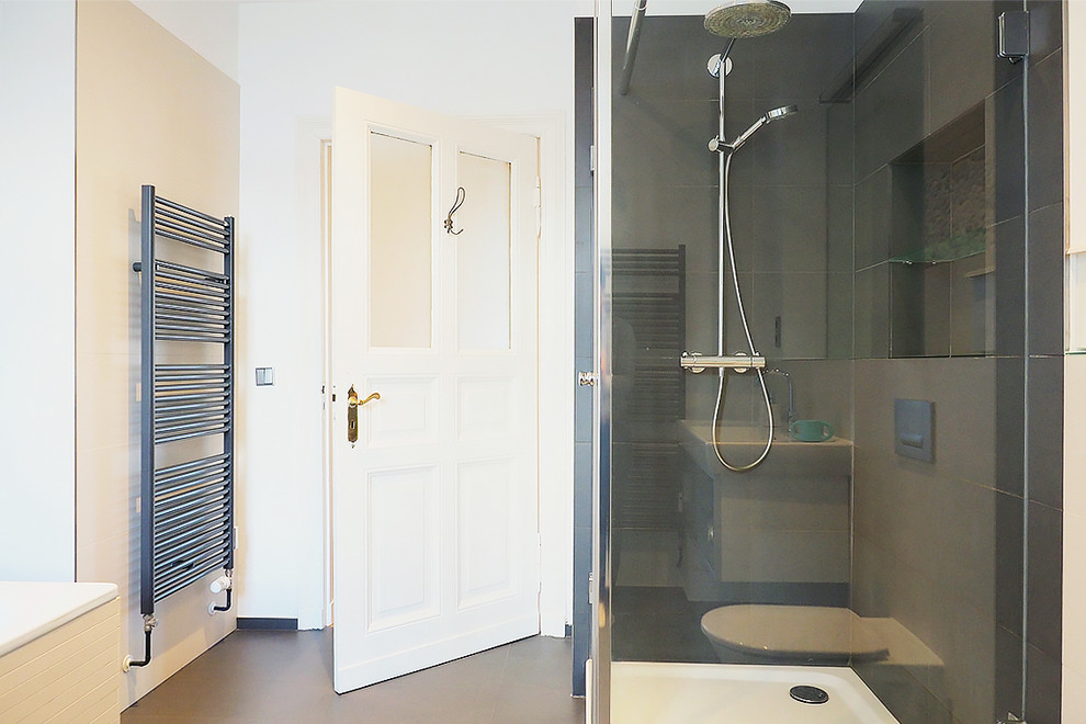 Large contemporary master bathroom in Berlin with glass-front cabinets, white cabinets, a freestanding tub, a corner shower, a wall-mount toilet, beige tile, ceramic tile, white walls, ceramic floors, a wall-mount sink and glass benchtops.