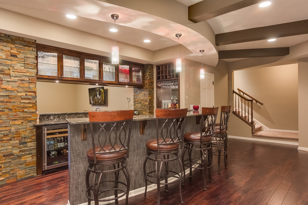 Design ideas for a mid-sized traditional u-shaped seated home bar in Minneapolis with an undermount sink, glass-front cabinets, dark wood cabinets, limestone benchtops, green splashback, stone tile splashback, dark hardwood floors, brown floor and brown benchtop.