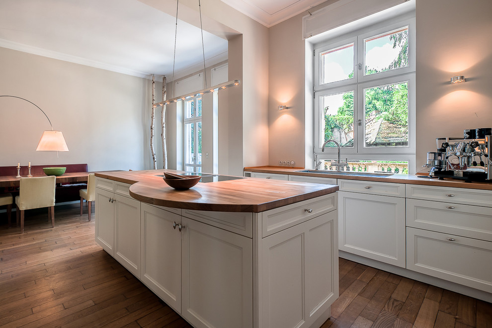 Mid-sized traditional open plan kitchen in Berlin with a drop-in sink, recessed-panel cabinets, white cabinets, wood benchtops, medium hardwood floors and with island.