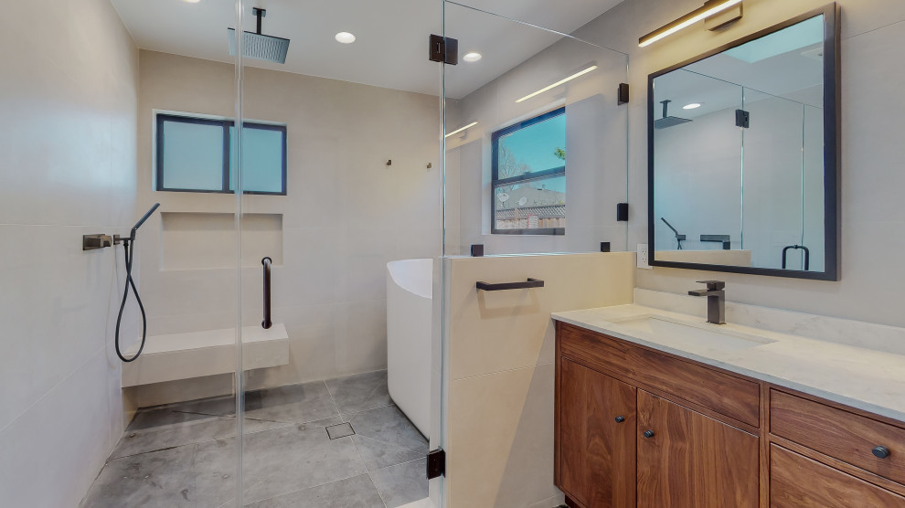 This is an example of a contemporary bathroom in San Francisco with medium wood cabinets, a freestanding tub, a shower/bathtub combo, beige tile, cement tile, beige walls, cement tiles, an undermount sink, marble benchtops, grey floor, a hinged shower door, multi-coloured benchtops, a double vanity and a built-in vanity.
