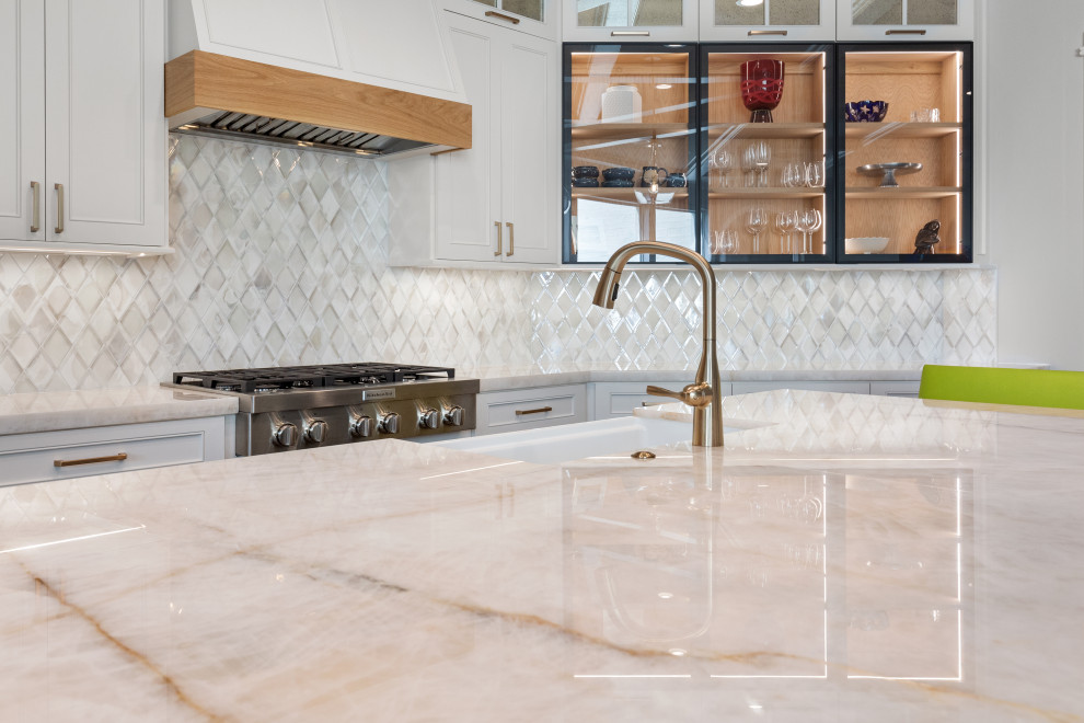 Large transitional single-wall light wood floor and brown floor eat-in kitchen photo in Houston with a farmhouse sink, recessed-panel cabinets, white cabinets, quartzite countertops, white backsplash, mosaic tile backsplash, stainless steel appliances, an island and white countertops