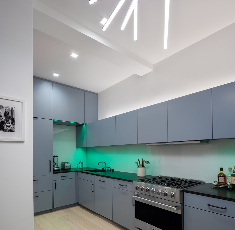Mid-sized contemporary l-shaped eat-in kitchen in New York with an undermount sink, flat-panel cabinets, blue cabinets, solid surface benchtops, black splashback, glass sheet splashback, coloured appliances, light hardwood floors, no island and beige floor.