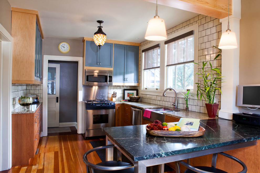 Example of a mid-sized eclectic galley light wood floor enclosed kitchen design with flat-panel cabinets, blue cabinets, stainless steel appliances, no island, an integrated sink and white backsplash