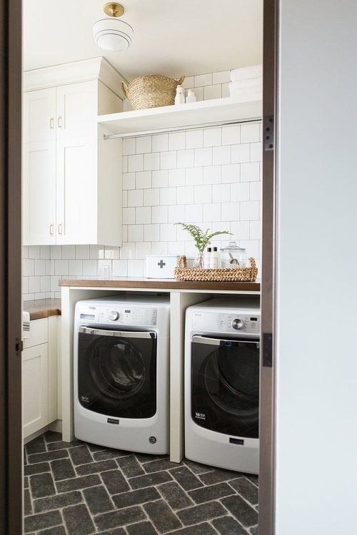 This is an example of a mid-sized eclectic laundry room in Salt Lake City with wood benchtops, white walls, brick floors, a side-by-side washer and dryer and black floor.