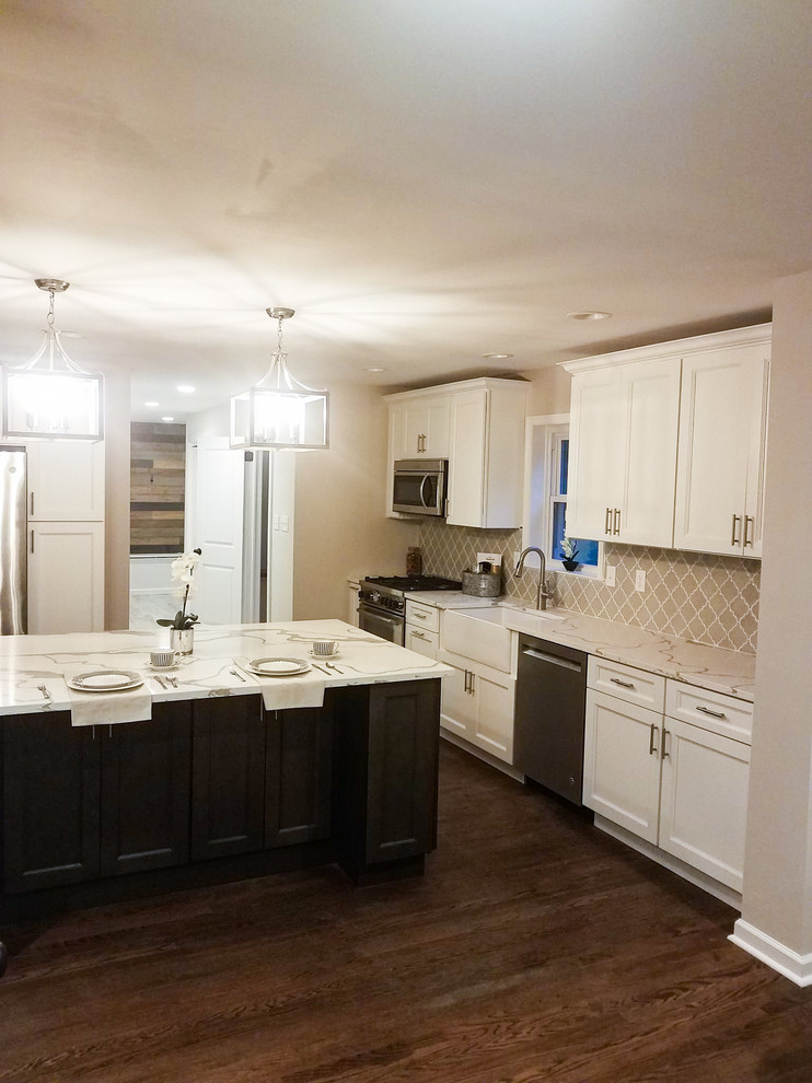 This is an example of a traditional kitchen in Philadelphia with a farmhouse sink, recessed-panel cabinets, white cabinets, granite benchtops, beige splashback, porcelain splashback, stainless steel appliances, dark hardwood floors, with island, brown floor and white benchtop.