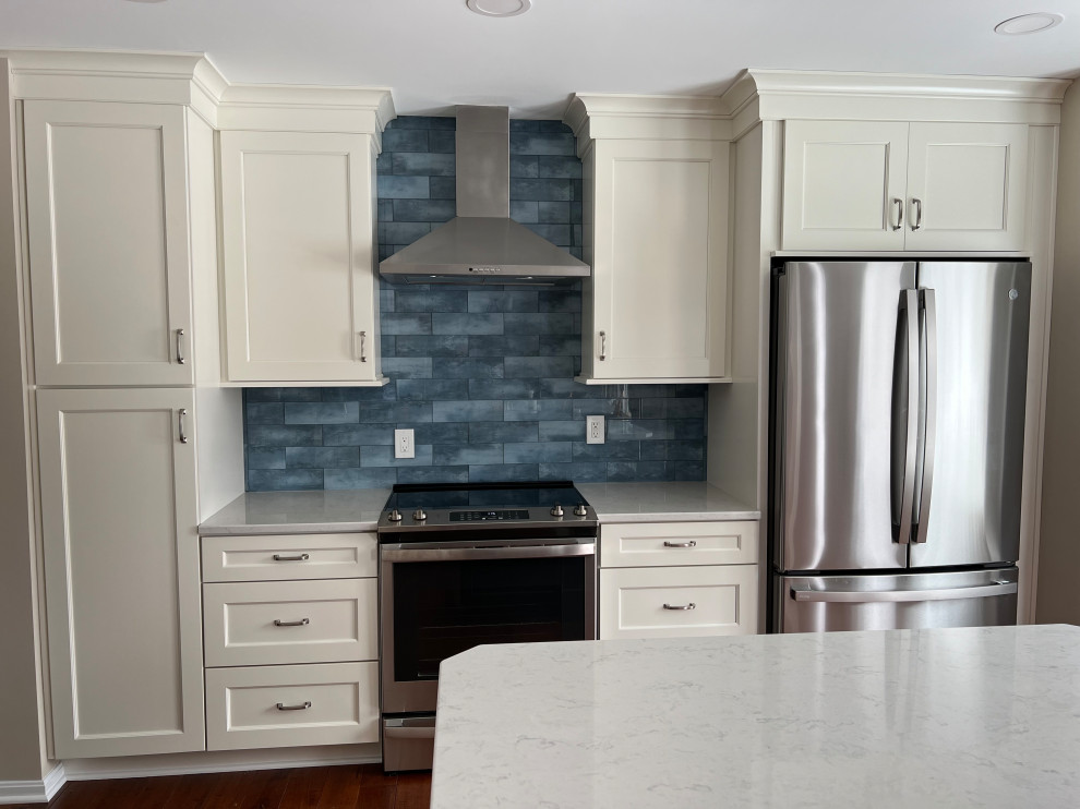 Example of a mid-sized transitional u-shaped medium tone wood floor and brown floor eat-in kitchen design in Cincinnati with an undermount sink, recessed-panel cabinets, white cabinets, quartz countertops, blue backsplash, glass tile backsplash, stainless steel appliances, an island and white countertops