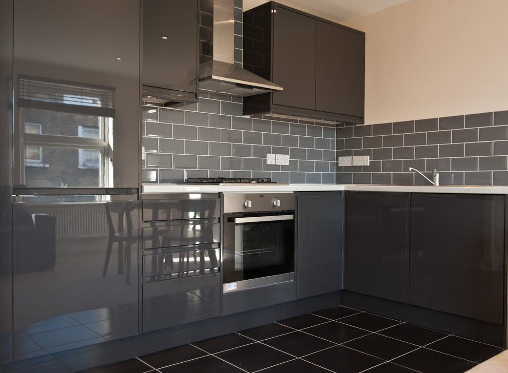 Photo of a large modern single-wall open plan kitchen in London with a drop-in sink, flat-panel cabinets, grey splashback, ceramic splashback, stainless steel appliances, ceramic floors, no island, black cabinets and quartz benchtops.