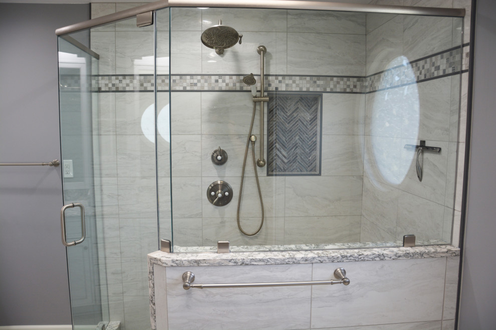 This is an example of a mid-sized transitional master bathroom in DC Metro with recessed-panel cabinets, white cabinets, a corner shower, a two-piece toilet, gray tile, grey walls, an undermount sink, engineered quartz benchtops, white floor, a hinged shower door, grey benchtops, a shower seat, a double vanity and a freestanding vanity.