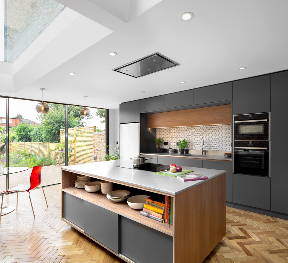 Photo of a scandinavian eat-in kitchen in Other with an integrated sink, flat-panel cabinets, grey cabinets, multi-coloured splashback, black appliances, light hardwood floors, with island and grey benchtop.