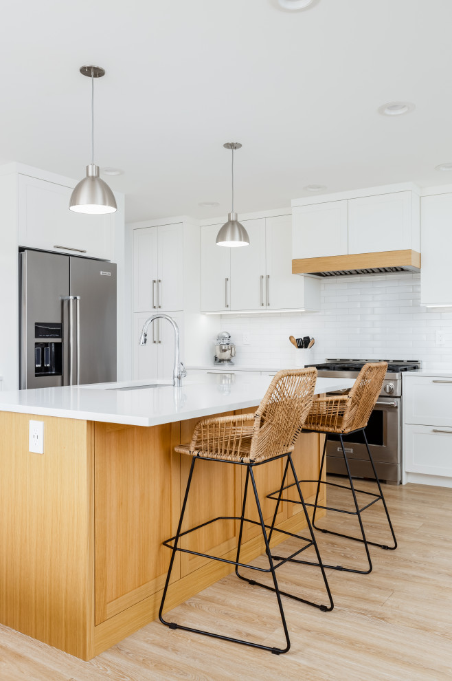 Mid-sized transitional l-shaped light wood floor and beige floor eat-in kitchen photo in Vancouver with an undermount sink, shaker cabinets, white cabinets, quartzite countertops, white backsplash, subway tile backsplash, stainless steel appliances, an island and white countertops