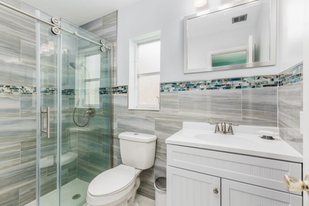 Photo of a small classic bathroom in Miami with shaker cabinets, white cabinets, a walk-in shower, a one-piece toilet, grey tiles, ceramic tiles, grey walls, porcelain flooring, a built-in sink, engineered stone worktops, grey floors, a sliding door, white worktops, a single sink and a built in vanity unit.