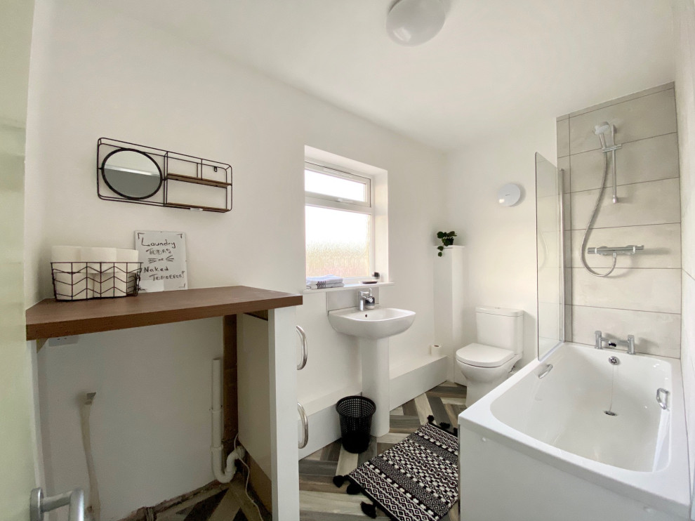Small contemporary master bathroom in Gloucestershire with a drop-in tub, a shower/bathtub combo, a one-piece toilet, gray tile, ceramic tile, white walls, linoleum floors, a pedestal sink, wood benchtops, multi-coloured floor, a hinged shower door, brown benchtops, a laundry and a single vanity.