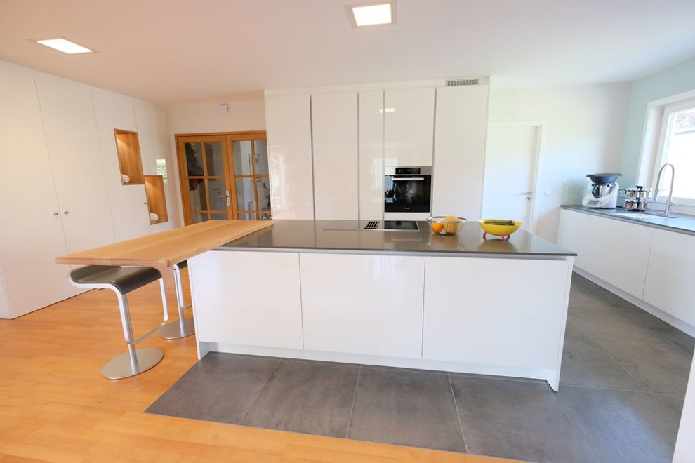 Inspiration for a mid-sized contemporary l-shaped open plan kitchen in Other with flat-panel cabinets, white cabinets, quartz benchtops, white splashback, stainless steel appliances, with island, grey benchtop, an integrated sink, ceramic floors and grey floor.