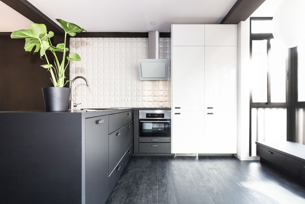 This is an example of a mid-sized contemporary l-shaped kitchen in Madrid with flat-panel cabinets, black cabinets, white splashback, stainless steel appliances, a peninsula and black floor.
