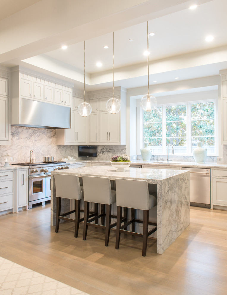 Transitional l-shaped kitchen in Other with white cabinets, white splashback, stainless steel appliances, light hardwood floors, with island and marble splashback.