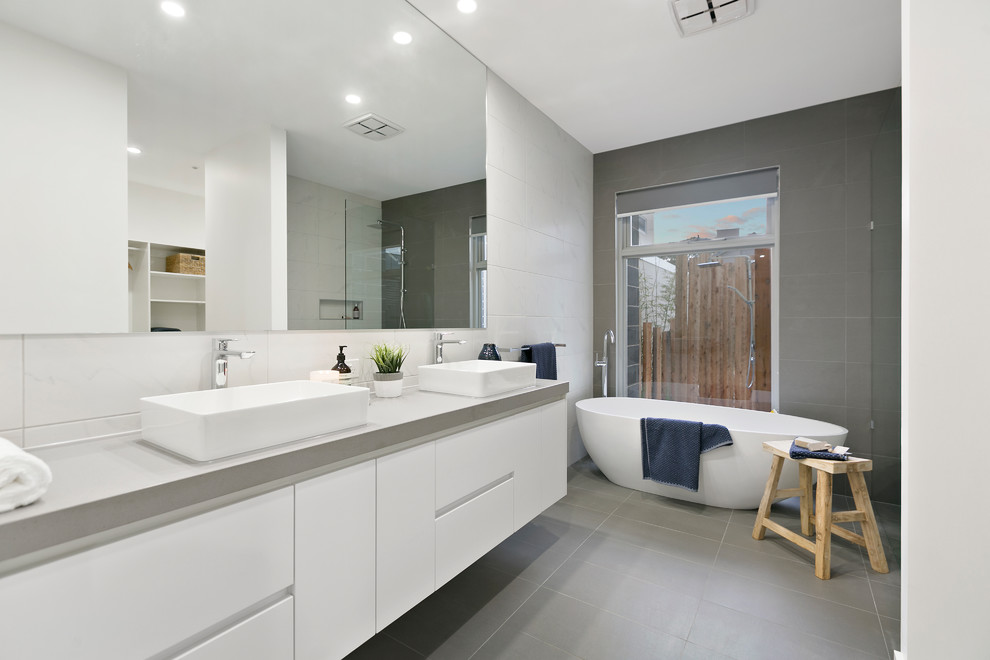 This is an example of a contemporary 3/4 bathroom in Melbourne with flat-panel cabinets, white cabinets, a freestanding tub, gray tile, white tile, a vessel sink, grey floor and grey benchtops.