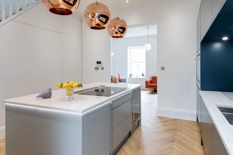 This is an example of a mid-sized contemporary single-wall open plan kitchen in London with a drop-in sink, stainless steel appliances, with island, white benchtop, flat-panel cabinets, blue cabinets, quartzite benchtops, white splashback and marble splashback.