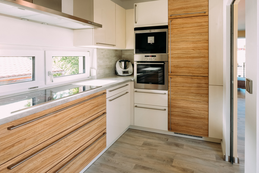 This is an example of a small contemporary l-shaped separate kitchen in Other with flat-panel cabinets, concrete benchtops, grey splashback, stainless steel appliances, light hardwood floors, no island, grey floor and grey benchtop.