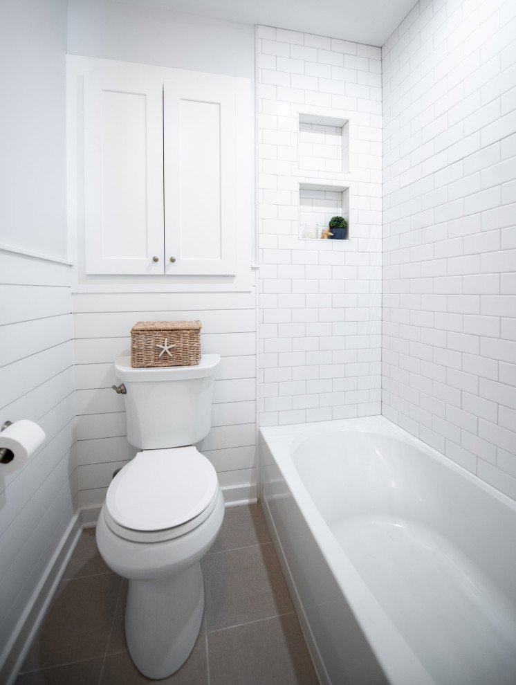 Photo of a small coastal ensuite bathroom in Philadelphia with shaker cabinets, white cabinets, an alcove bath, a shower/bath combination, a two-piece toilet, grey tiles, stone tiles, ceramic flooring, a submerged sink, engineered stone worktops, a shower curtain, white worktops, a wall niche, a single sink, a built in vanity unit and tongue and groove walls.