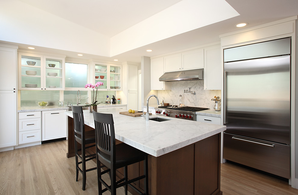 Photo of a contemporary l-shaped kitchen in San Francisco with glass-front cabinets, stainless steel appliances, a single-bowl sink, white cabinets, marble benchtops, white splashback and stone slab splashback.