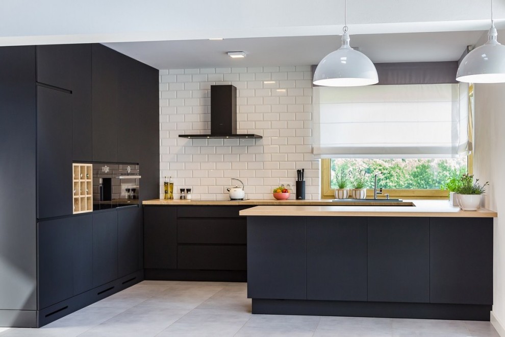 Inspiration for a contemporary u-shaped gray floor kitchen remodel with flat-panel cabinets, black cabinets, wood countertops, white backsplash, subway tile backsplash, black appliances and a peninsula