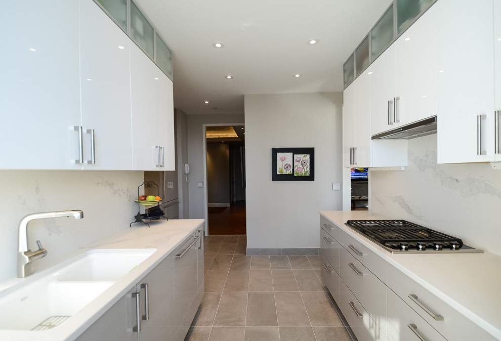 Photo of a large contemporary galley separate kitchen in New York with a farmhouse sink, flat-panel cabinets, grey cabinets, quartzite benchtops, white splashback, stainless steel appliances, porcelain floors, no island, grey floor and white benchtop.