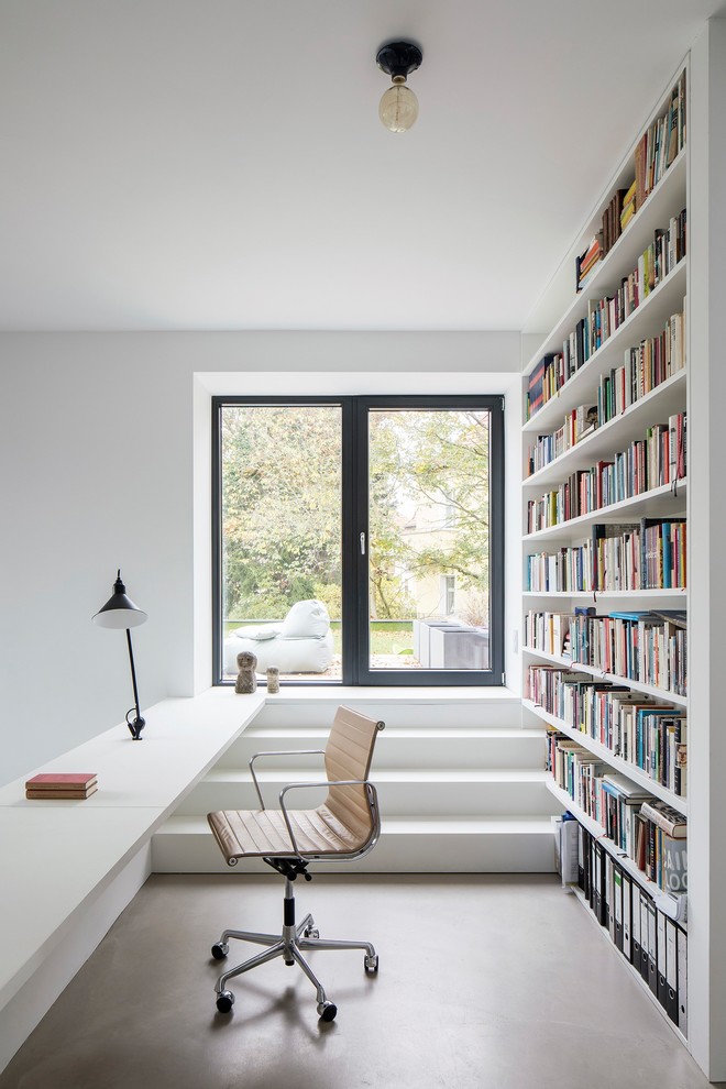 Inspiration for a small contemporary home office in Berlin with a library, white walls, concrete floors, a built-in desk and grey floor.