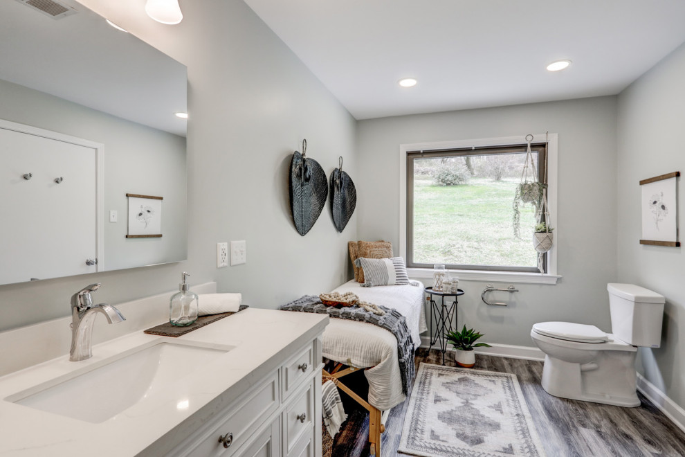 This is an example of a large transitional master bathroom in Other with recessed-panel cabinets, white cabinets, a shower/bathtub combo, a two-piece toilet, grey walls, vinyl floors, an undermount sink, quartzite benchtops, grey floor, a shower curtain, white benchtops, a single vanity and a freestanding vanity.