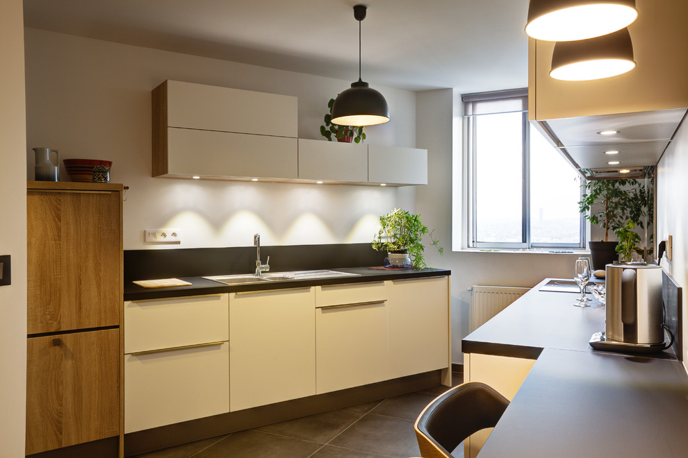 Réalisation d'une cuisine ouverte parallèle et encastrable design de taille moyenne avec un évier 1 bac, un placard à porte plane, des portes de placard blanches, un plan de travail en stratifié, une crédence noire, sol en béton ciré, aucun îlot et un sol gris.