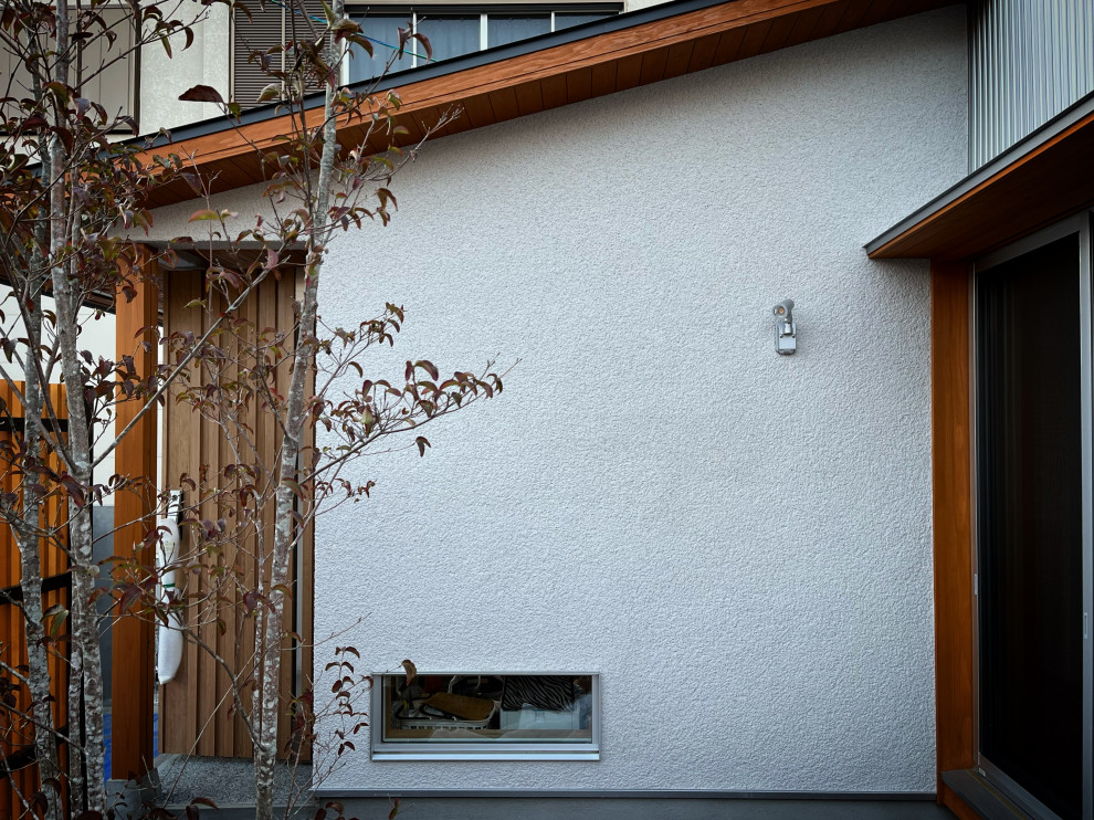На фото: маленький, двухэтажный, белый частный загородный дом с облицовкой из цементной штукатурки, двускатной крышей, металлической крышей, черной крышей и отделкой доской с нащельником для на участке и в саду