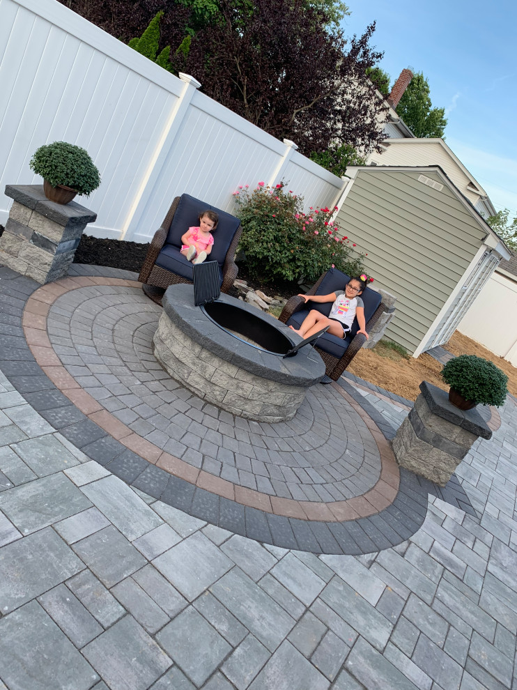 Large backyard patio in New York with a fire feature and concrete pavers.