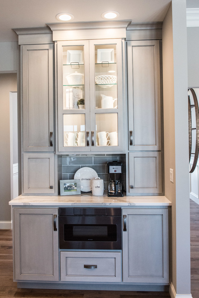 Example of a huge transitional l-shaped medium tone wood floor and brown floor open concept kitchen design with a single-bowl sink, glass-front cabinets, gray cabinets, quartz countertops, gray backsplash, ceramic backsplash, stainless steel appliances, an island and white countertops