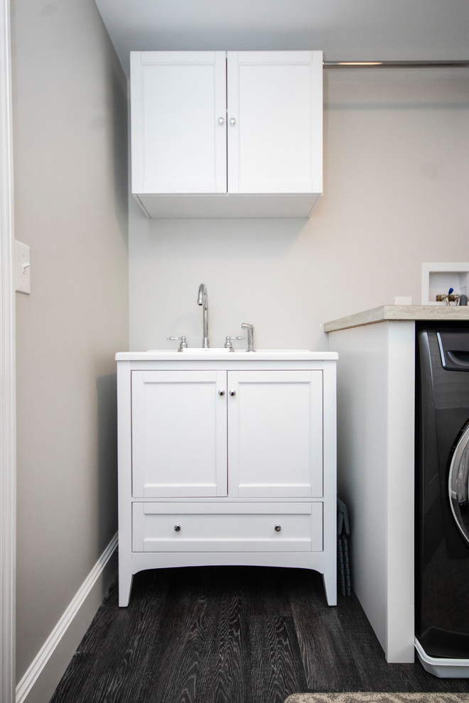 Mid-sized transitional single-wall dedicated laundry room in Boston with a drop-in sink, recessed-panel cabinets, white cabinets, laminate benchtops, grey walls, vinyl floors, a side-by-side washer and dryer, grey floor and brown benchtop.