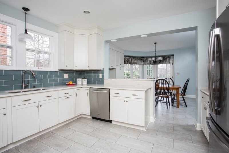 This is an example of a mid-sized transitional u-shaped eat-in kitchen in Other with an undermount sink, shaker cabinets, white cabinets, quartz benchtops, blue splashback, glass tile splashback, stainless steel appliances, vinyl floors and a peninsula.