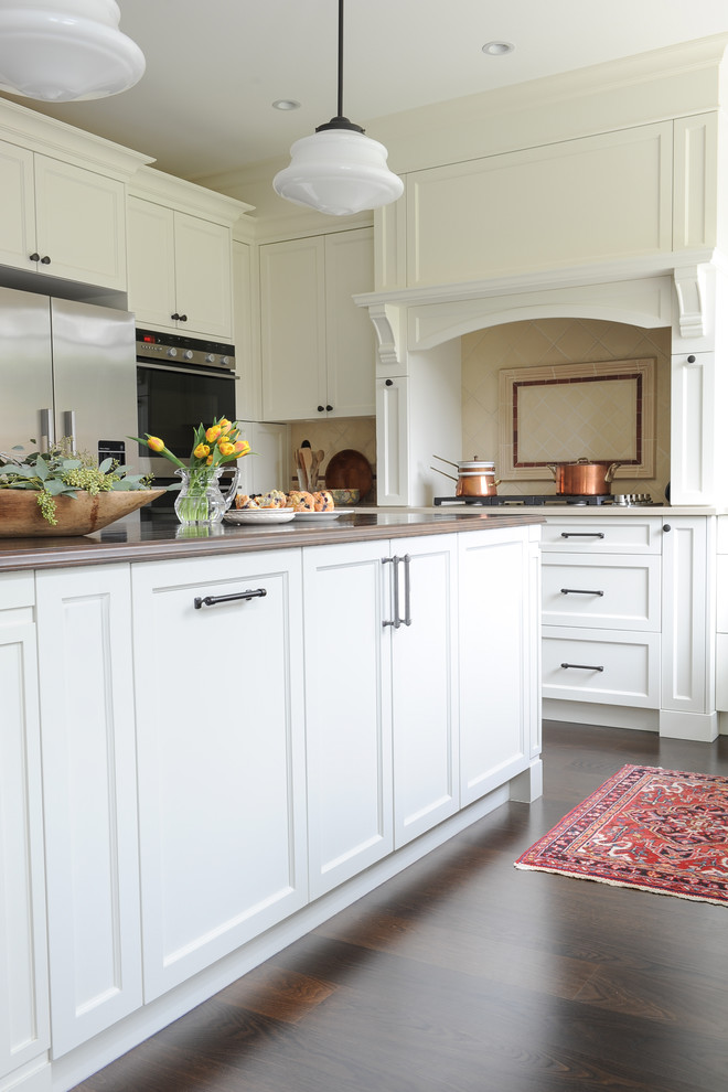 Example of a mid-sized transitional u-shaped dark wood floor enclosed kitchen design in Vancouver with an undermount sink, recessed-panel cabinets, white cabinets, wood countertops, beige backsplash, terra-cotta backsplash, stainless steel appliances and an island