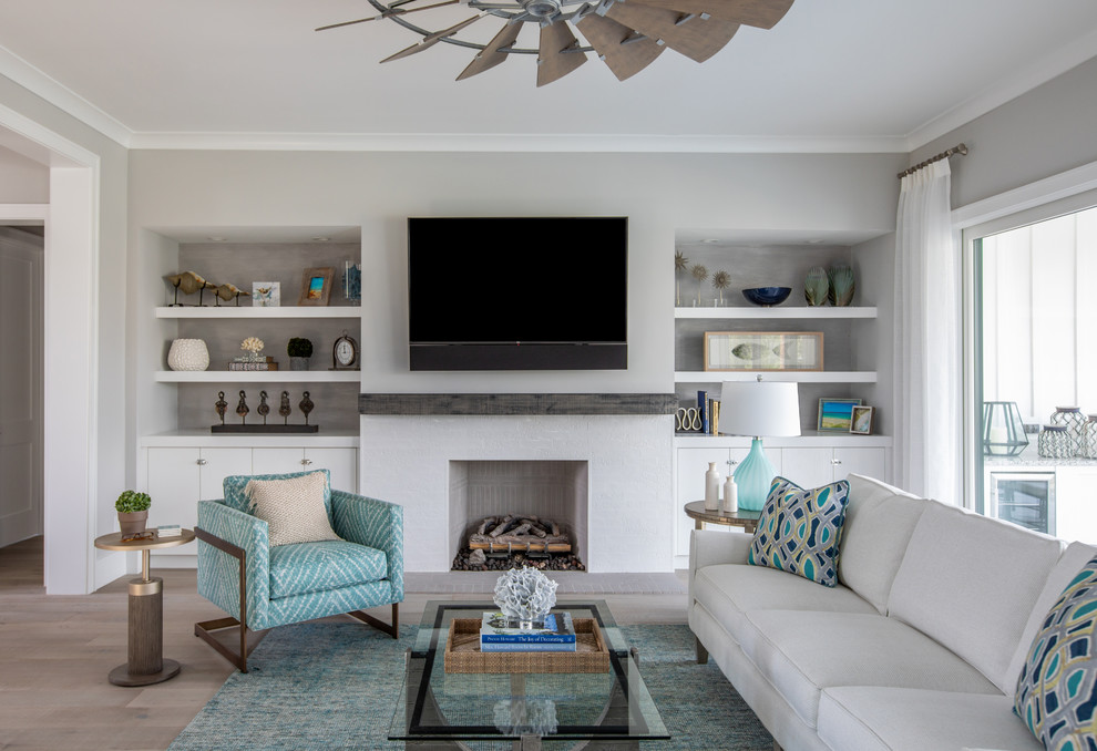 Inspiration for a beach style family room in Jacksonville with grey walls, light hardwood floors, a standard fireplace, a wall-mounted tv and beige floor.