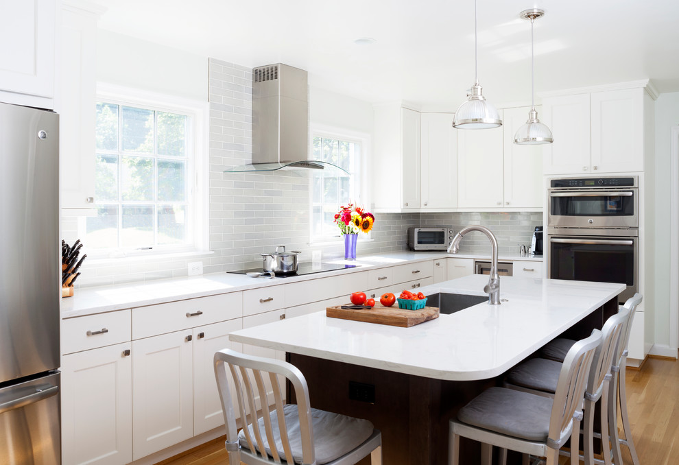 Design ideas for a mid-sized transitional l-shaped eat-in kitchen in DC Metro with white cabinets, quartz benchtops, grey splashback, subway tile splashback, stainless steel appliances, medium hardwood floors and with island.
