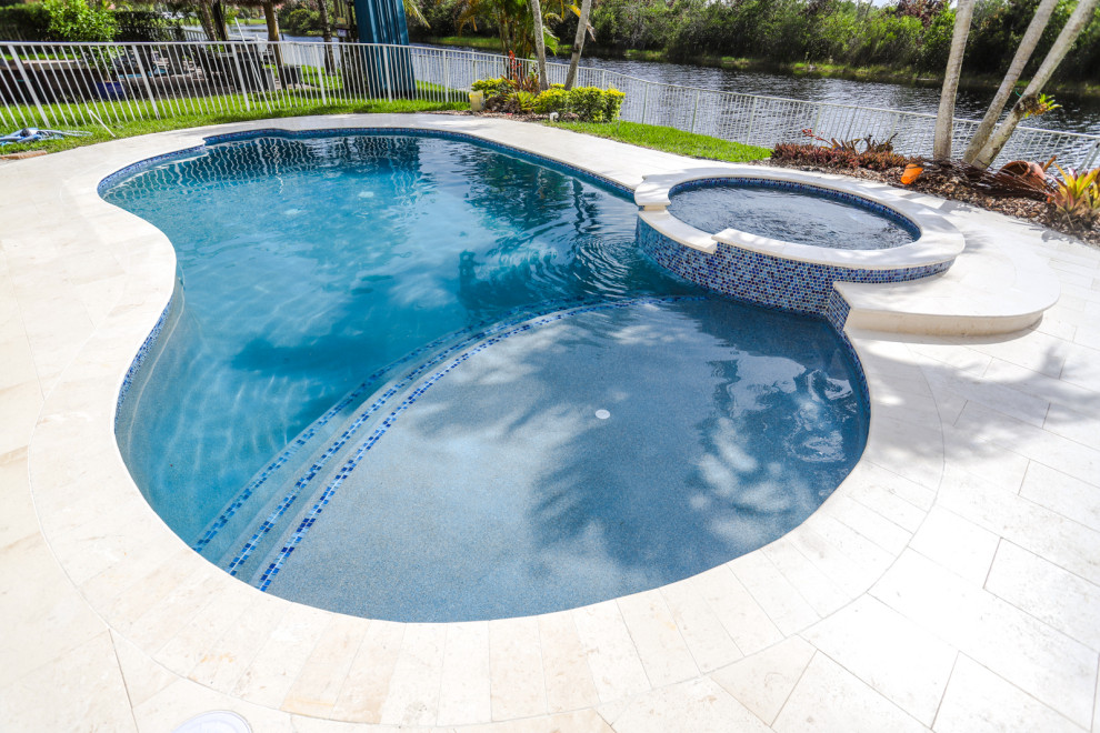Moderner Whirlpool hinter dem Haus in Nierenform mit Natursteinplatten in Miami