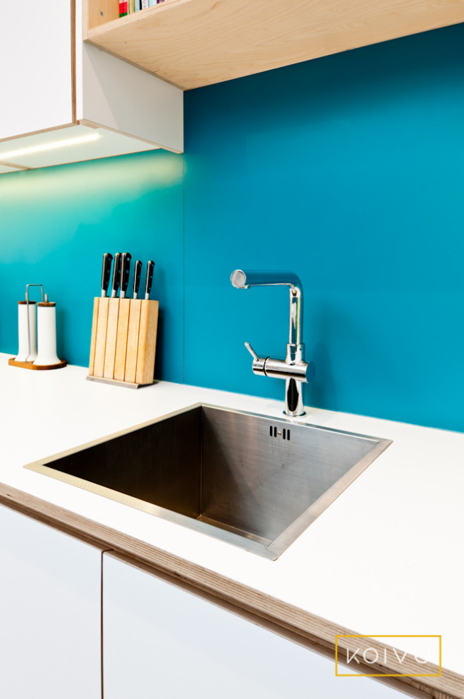 Inspiration for a mid-sized contemporary single-wall eat-in kitchen in Wiltshire with flat-panel cabinets, turquoise cabinets, laminate benchtops, blue splashback, panelled appliances, porcelain floors, with island, grey floor and white benchtop.