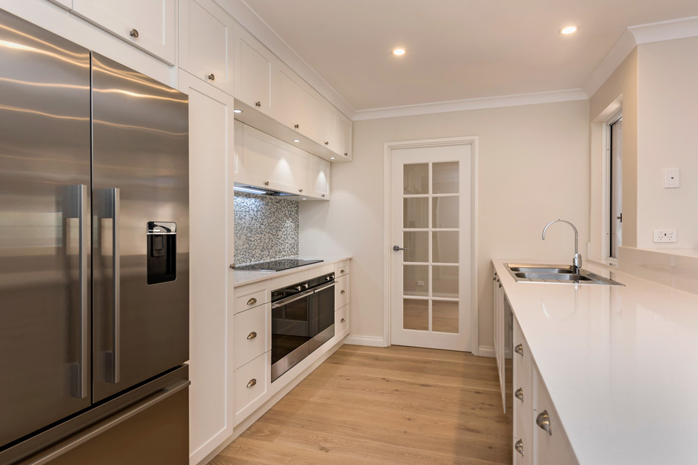 Inspiration for a mid-sized beach style kitchen in Perth with shaker cabinets, white cabinets, quartz benchtops, multi-coloured splashback, light hardwood floors, a peninsula and white benchtop.