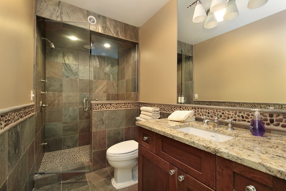 Mid-sized traditional 3/4 bathroom in Jacksonville with recessed-panel cabinets, dark wood cabinets, an alcove shower, a one-piece toilet, brown tile, pebble tile, beige walls, limestone floors, an undermount sink, granite benchtops, multi-coloured floor and a hinged shower door.