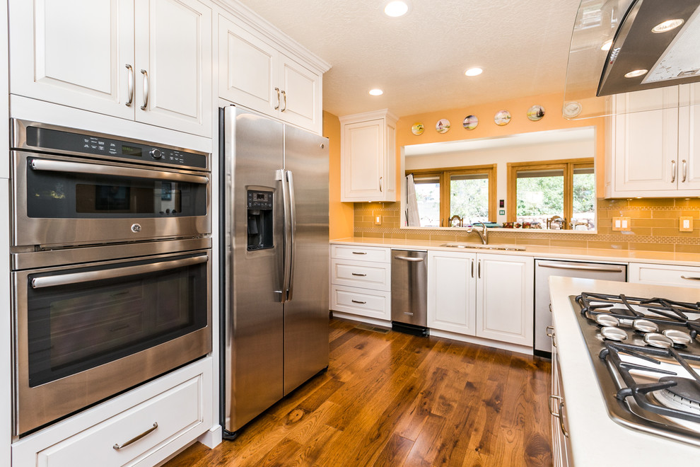 Inspiration for a mid-sized transitional u-shaped medium tone wood floor enclosed kitchen remodel in Albuquerque with white cabinets, quartz countertops, beige backsplash, subway tile backsplash, stainless steel appliances, an island, a double-bowl sink and raised-panel cabinets