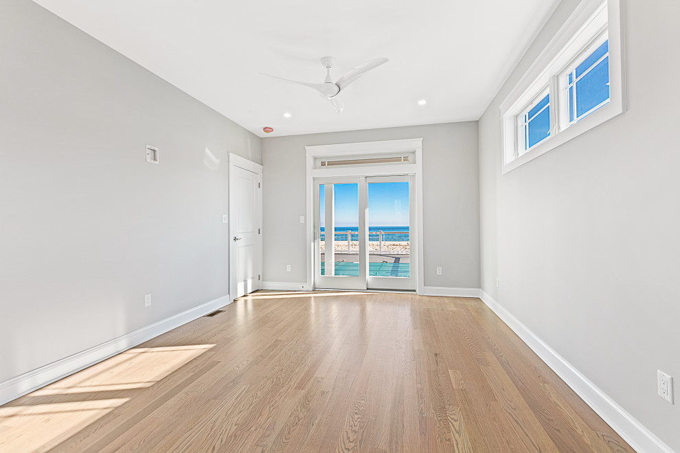 Photo of a beach style guest bedroom in New York with grey walls, light hardwood floors and beige floor.